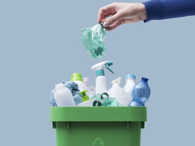 Woman putting a plastic bottle in a full recycling bin.