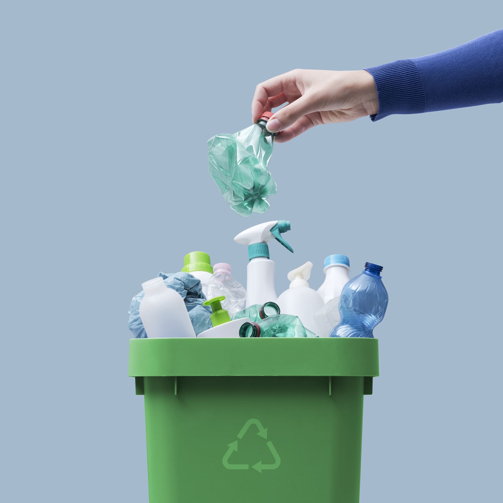 Woman putting a plastic bottle in a full recycling bin.