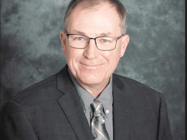 Ken Foster wearing a dark grey suit with a grey backdrop Technology Manager